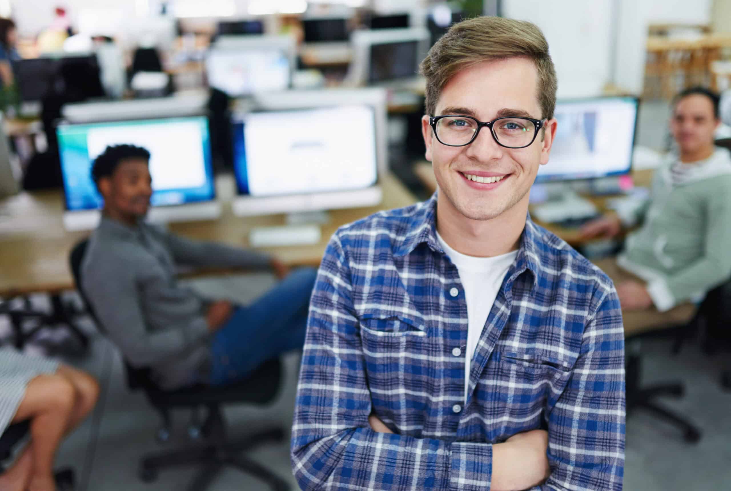 Person im karierten Hemd lächelt in einem modernen Büro vor Monitoren