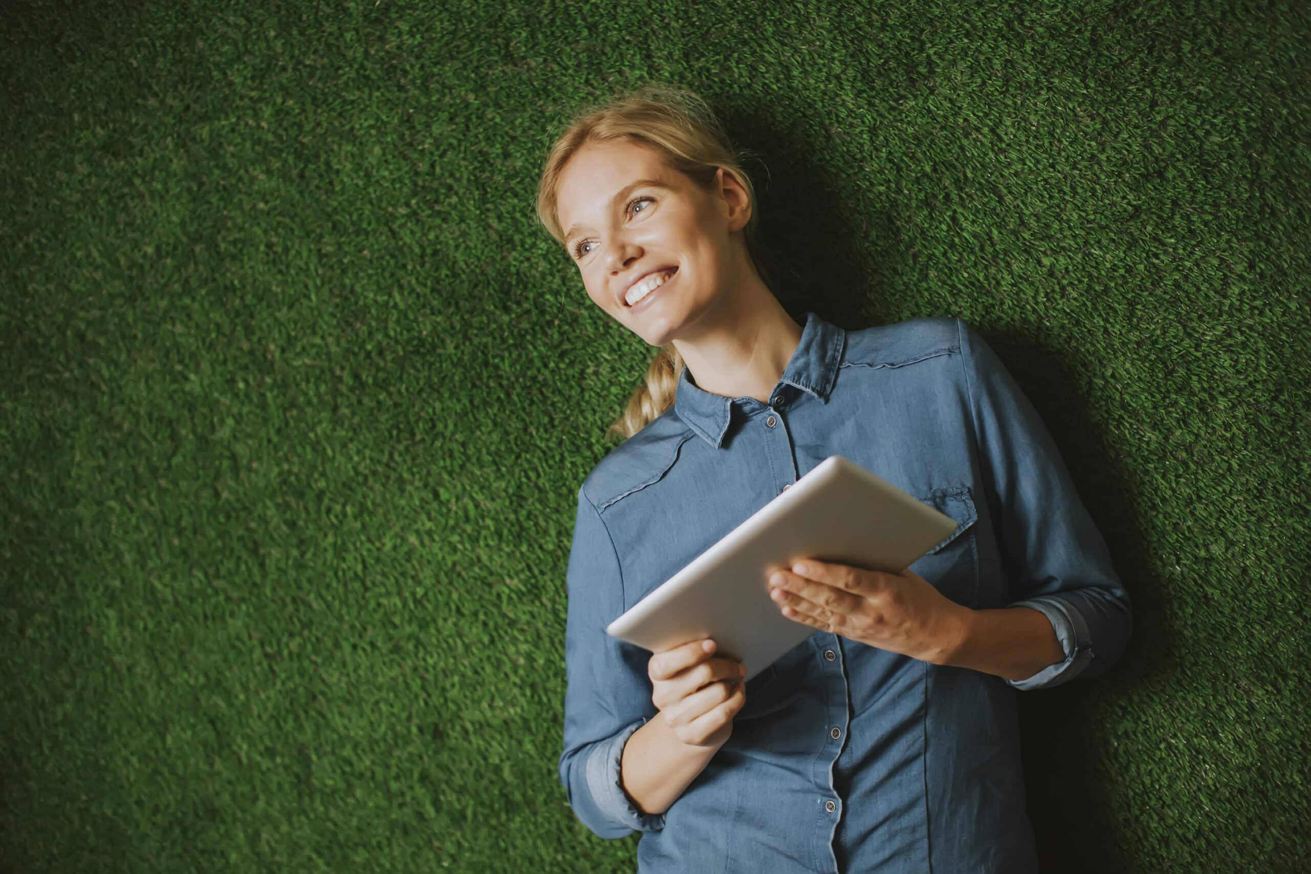 Frau liegt im Gras und hält ein Tablet – Green IT