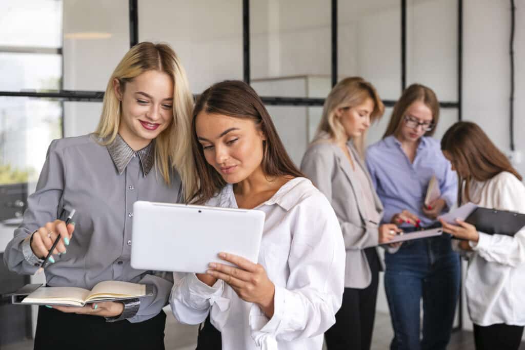 Zwei Frauen schauen auf ein Tablet und besprechen Notizen in einem modernen Büro