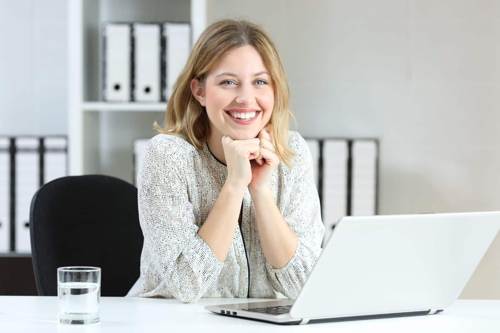Lächelnde Frau sitzt an einem Schreibtisch und arbeitet am Laptop