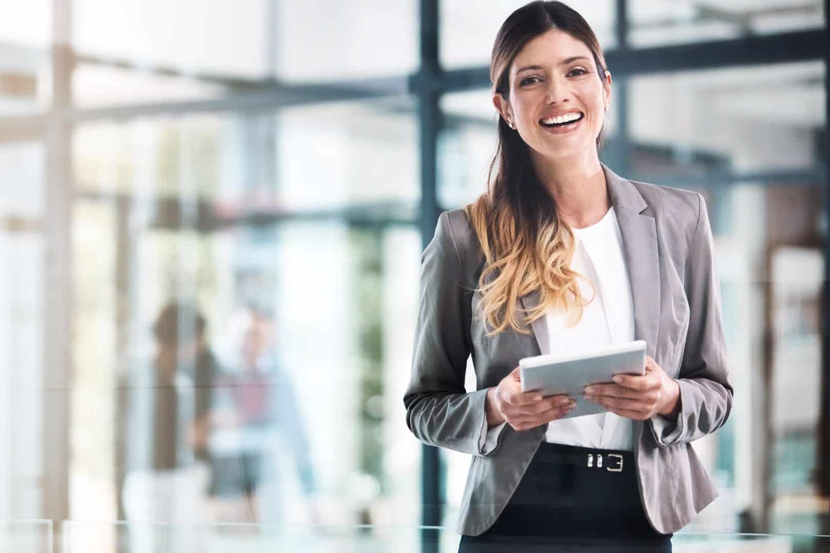Lächelnde Frau in Businesskleidung hält ein Tablet im modernen Büro