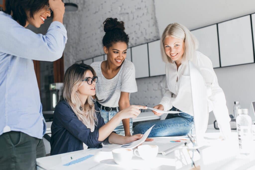 Vier junge Frauen arbeiten gemeinsam am Tisch und besprechen Dokumente