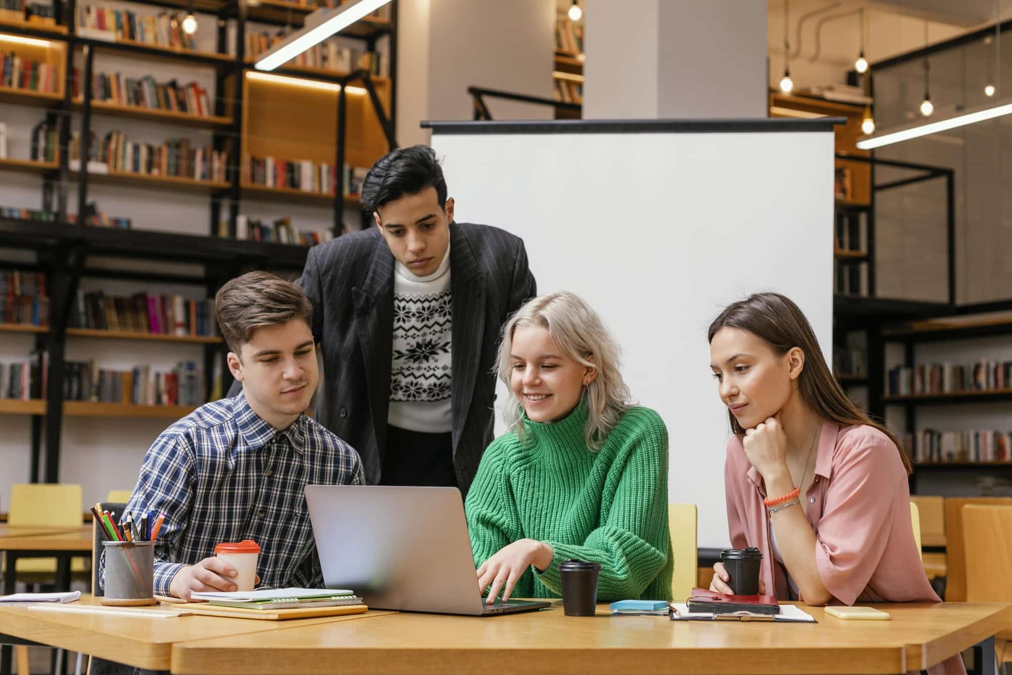 Gruppe junger Menschen arbeitet gemeinsam an einem Laptop in einer Bibliothek