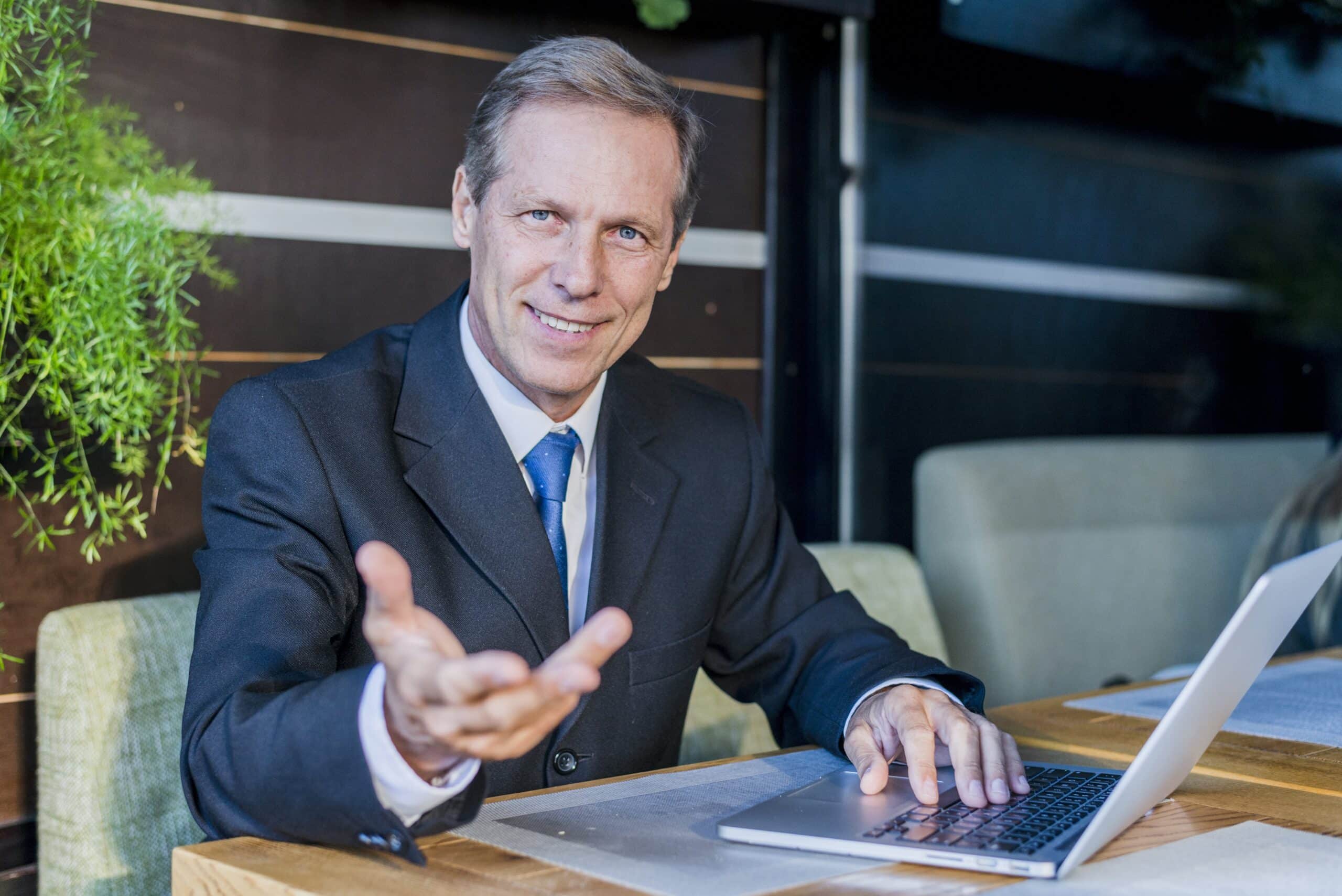 Geschäftsmann im Anzug arbeitet an einem Laptop und gestikuliert lächelnd