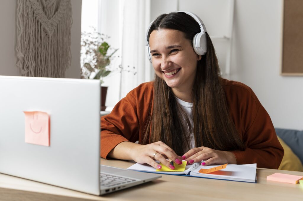 Junge Frau mit Kopfhörern sitzt am Laptop und lächelt während der Arbeit