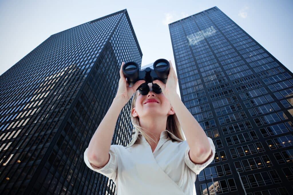 Business-Ökosysteme: Businessfrau mit Fernglas vor modernen Hochhäusern