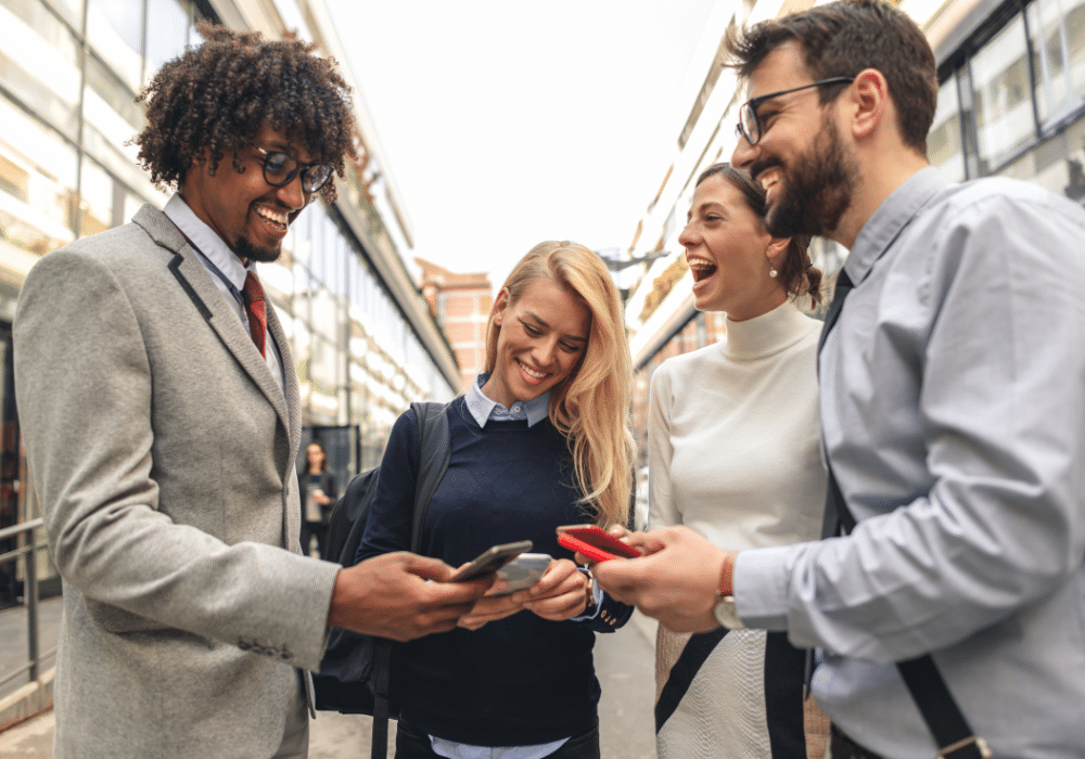 Gruppe junger Kollegen, die gemeinsam auf ihre Smartphones schauen und lachen