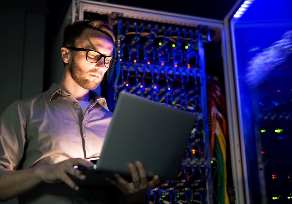 IT-Techniker arbeitet mit Laptop vor Serverschrank in einem Rechenzentrum zur Überprüfung von Cybersecurity-Systemen